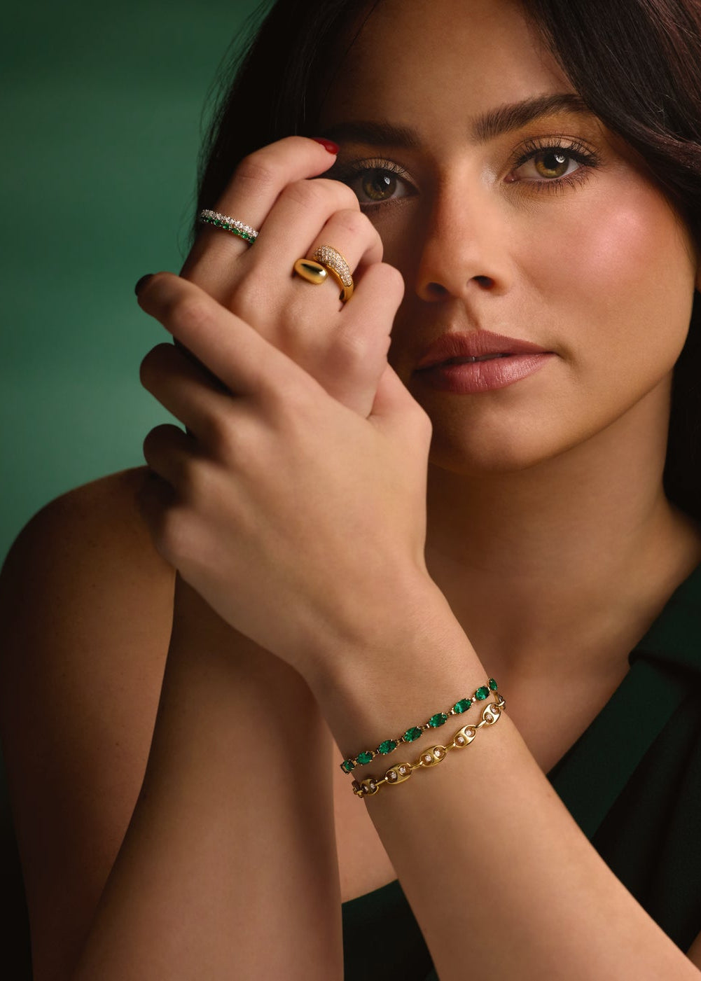 Woman wearing gold and green jewelry against a dark background